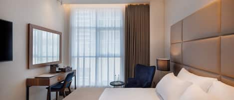 A hotel room with a large bed, a desk with a chair, a television, and a window with curtains.