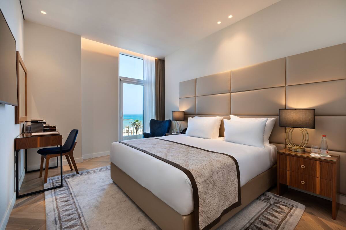 A modern hotel room with a large bed, a desk, and a view of the ocean.