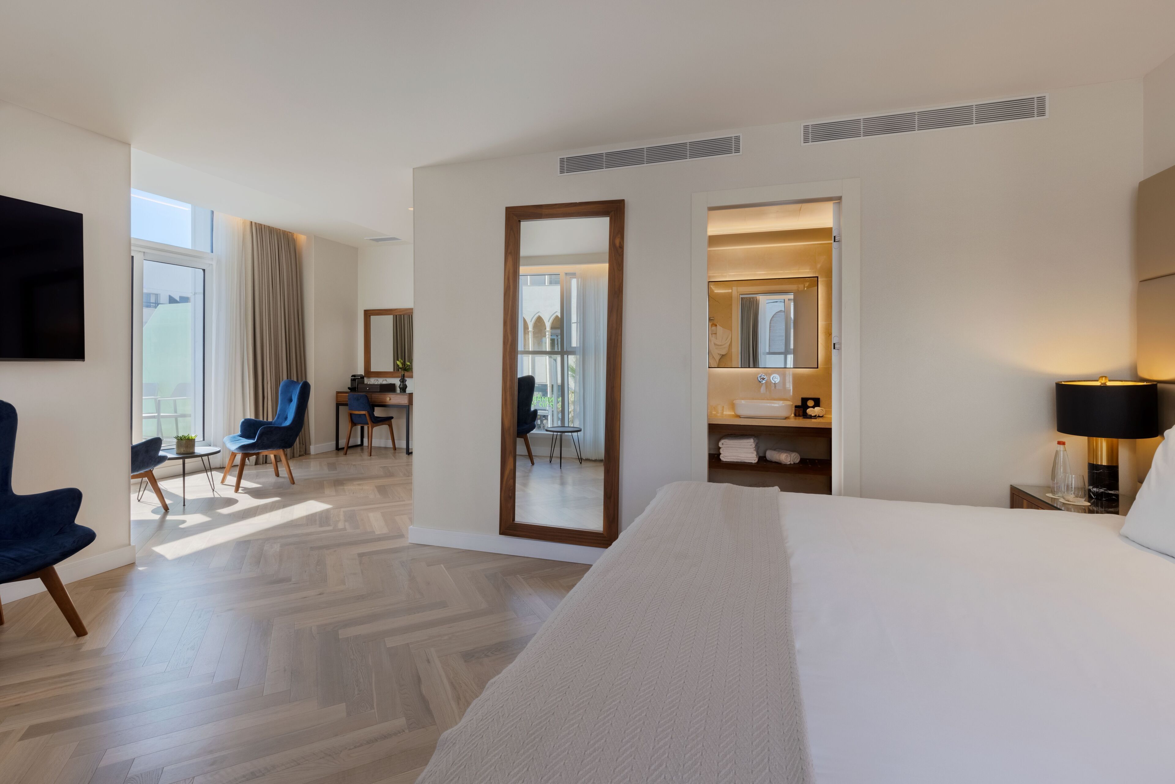 A hotel room with a large bed, a desk, a chair, a mirror, and a TV.
