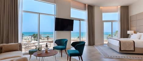 Habitación de hotel con un ventanal grande, una cama, un televisor y una zona de estar con una mesa y sillas.