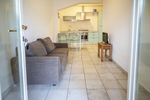 Ein Wohnzimmer mit einer Couch, einem Esstisch mit Stühlen, einer Küchenzeile inklusive Schränken und Herd sowie einem kleinen Holztisch mit Fernseher.