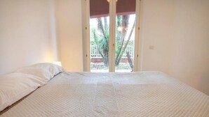 A bedroom with a bed, a window, and a view of palm trees. - S102 - Sirolo, new three-room apartment with garden (Sirolo)