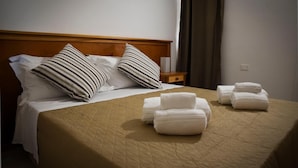 Una cama bien hecha con almohadillas a rayas, una colcha acolchada y toallas enrolladas sobre la cama.