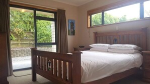A bedroom with a wooden bed, a nightstand, a window with curtains, and a view of greenery outside. - View from Fletcher Street (Taupo)