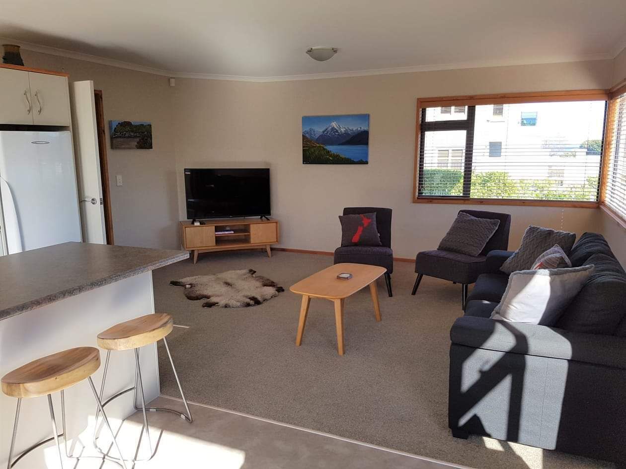 A modern living room with a sofa, two armchairs, a coffee table, a TV, and a kitchen area with a fridge.