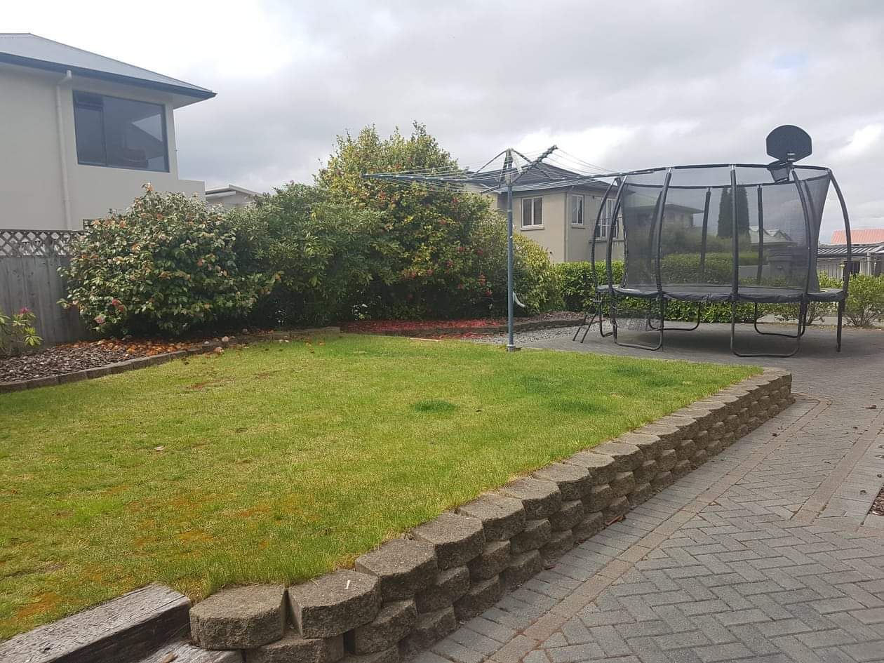 A residential garden with a lawn, a stone wall, and a metal structure.