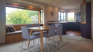 A modern kitchen with a dining area, large windows, and a view of greenery. - View from Fletcher Street (Taupo)