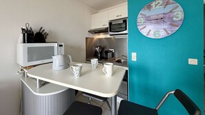 A compact kitchenette with a microwave, kettle, and coffee maker on a white countertop. A teal wall features a clock. - 2-room apartment, sea view balcony, private parking, Demoiselles Beach (Saint-Hilaire-de-Riez)