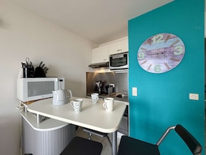 A compact kitchenette with a microwave, kettle, and coffee maker on a white countertop. A teal wall features a clock. - 2-room apartment, sea view balcony, private parking, Demoiselles Beach (Saint-Hilaire-de-Riez)