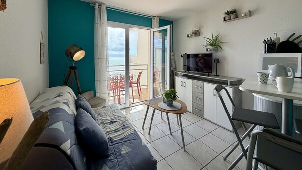 Un espacio habitable pequeño con sofá, una mesa de comedor, televisor y balcón con vistas.