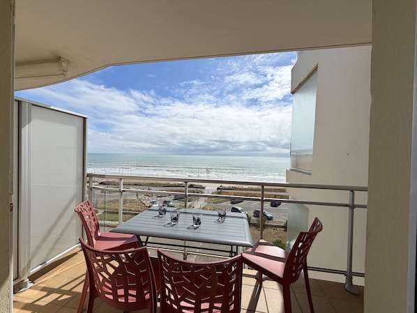A balcony with a table and chairs, overlooking a beach and ocean.