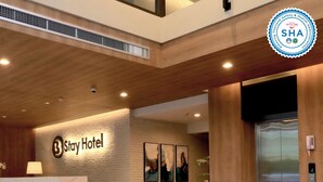 A hotel lobby with a reception desk, two sofas with blue cushions, a coffee table, and a wall-mounted elevator. - B Stay Hotel (Bangkok)