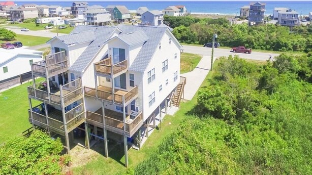 Een tweelaags huis met balkon en terras, nabij een strand met andere huizen en een helder uitzicht op zee.
