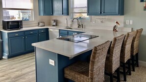 Een moderne keuken met blauwe kastjes, een centraal eiland en een eetgedeelte met rieten stoelen.