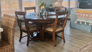 Een eethoek met een houten tafel en stoelen, een klok aan de muur en een televisie op de achtergrond.
