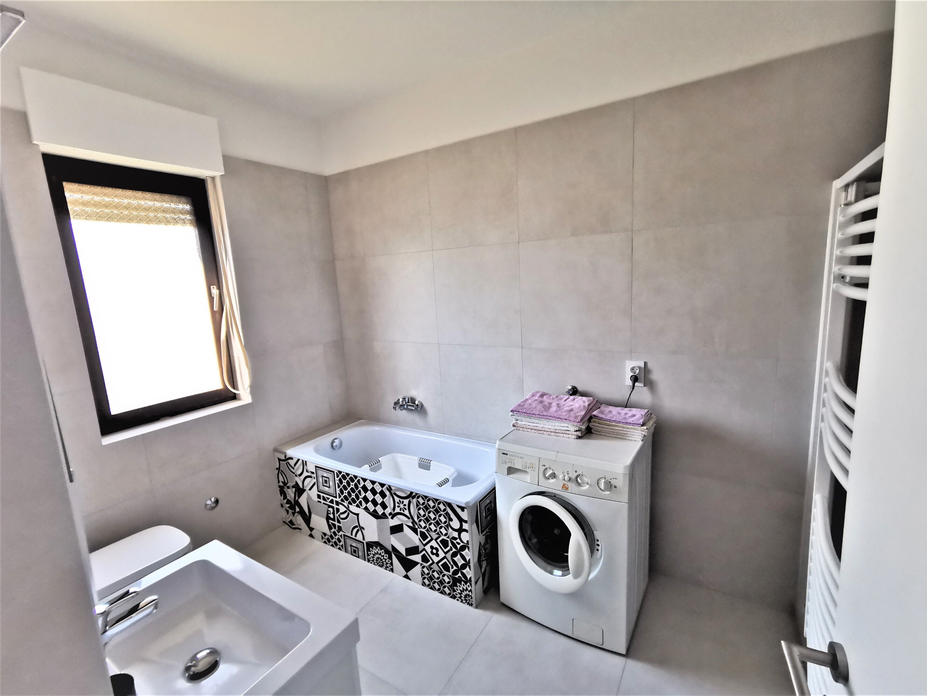 Een kleine badkamer met een bad, een wasmachine en een wastafel.