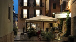 An outdoor café area with a large umbrella, potted plants, and a sign for 'Gabrielle Ristorante'.