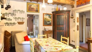 A dining area with a table set for two, a radiator, a sofa with a red cushion, and a wooden cabinet. - 4 bed apartment with pool (Pontremoli)