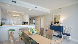 A dining area with a glass table, wicker chairs, and a central floral arrangement. - Navarre Beach Regency 304 - Eat. Beach. Sleep. Repeat. (Navarre)