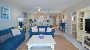 A spacious living room with a blue sofa, a white coffee table, and a television on a cabinet. - Navarre Beach Regency 304 - Eat. Beach. Sleep. Repeat. (Navarre)