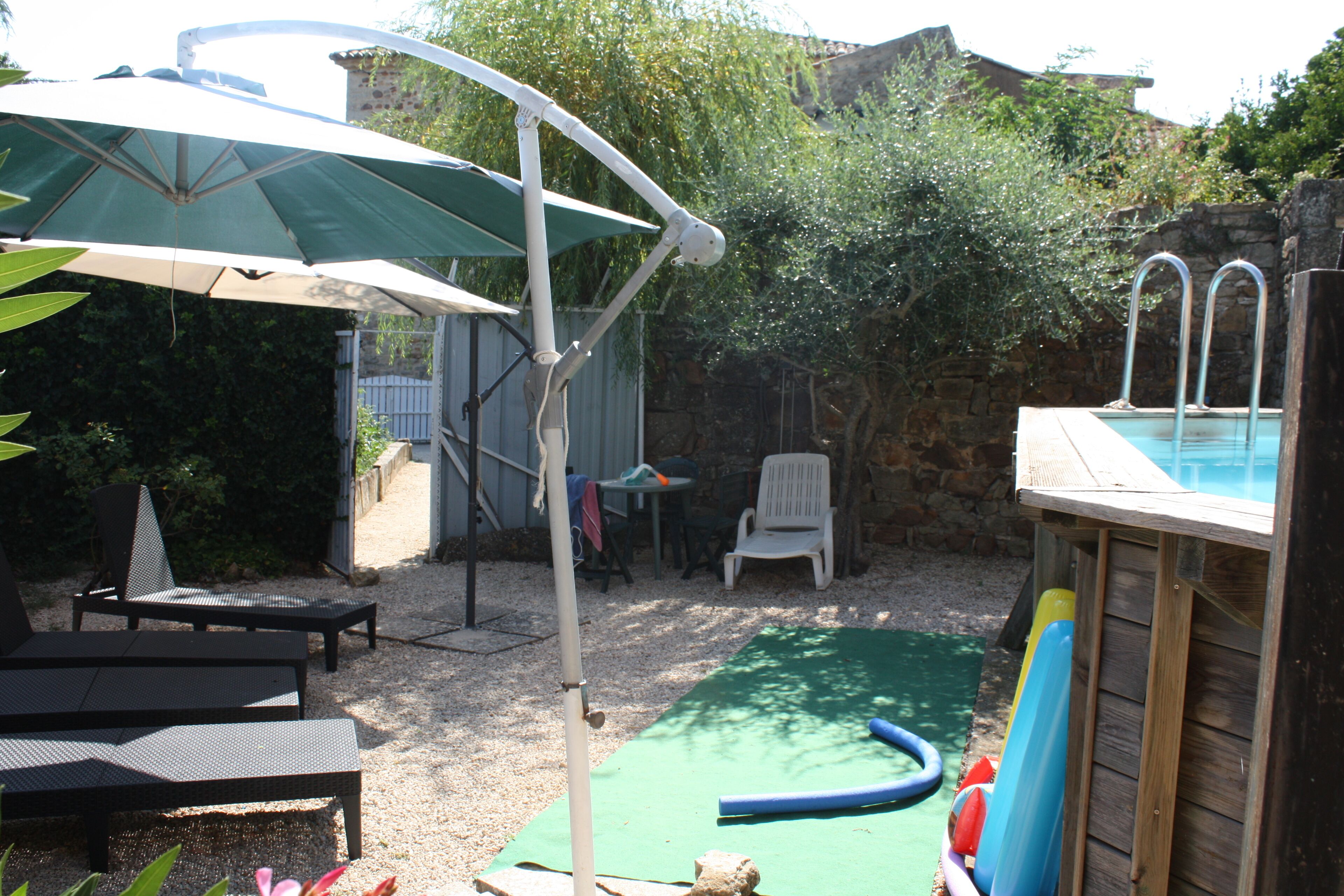 Een buitenzwembad met een glijbaan, ligbedden en een tafel onder een grote parasol.