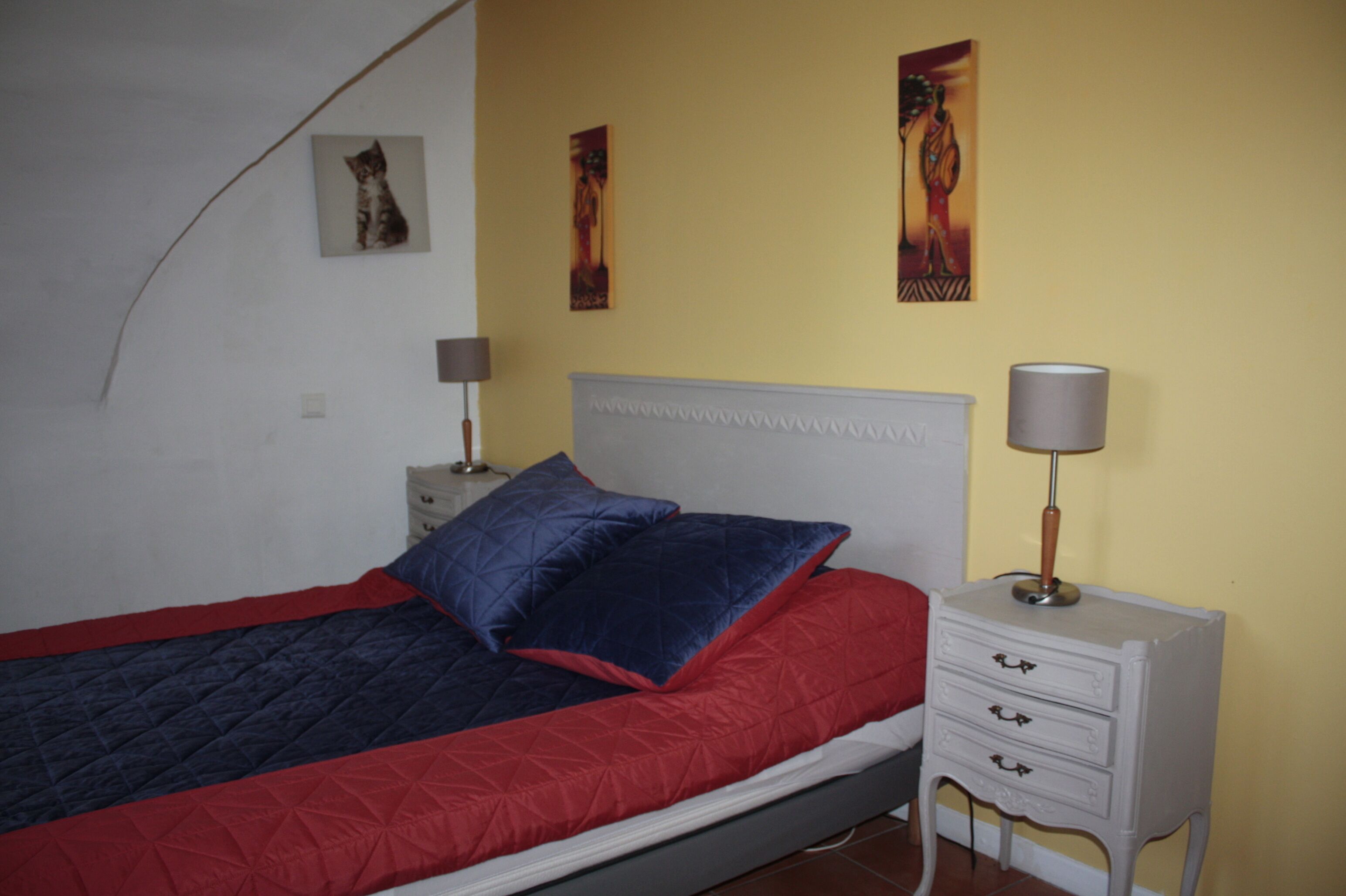 Une chambre à coucher avec un lit, une table de chevet, une lampe et des œuvres d’art murales.