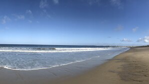 A beach with waves reaching the shore, a clear sky, and distant land.