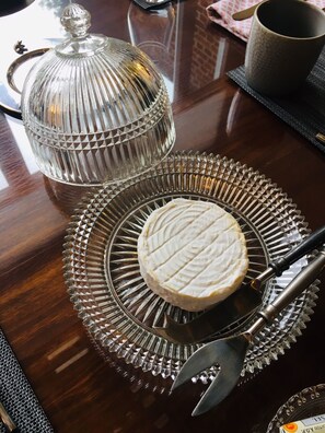 A table with a glass cheese wheel, a cheese knife, and a glass cheese slicer. - Les Chambres d'Hôtes du Palais (Douai)
