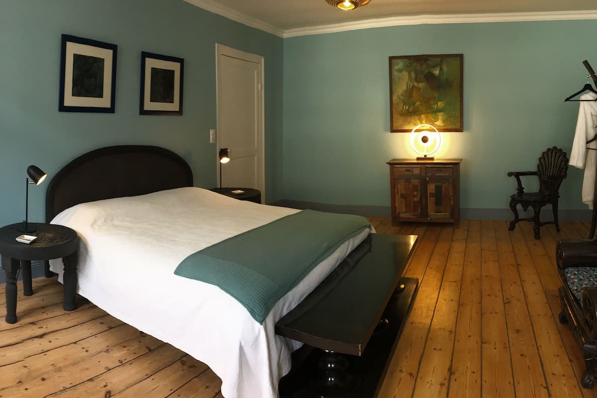 A bedroom with a bed, bedside tables, a bench, a lamp, a painting, and a coat rack.