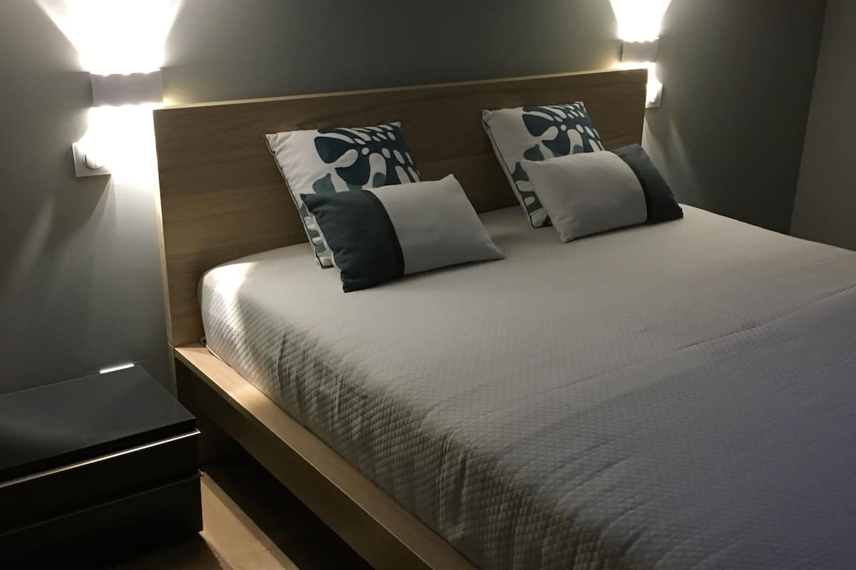A modern bedroom with a wooden headboard, two bedside lamps, a bedside table, and a bed with a quilted cover.