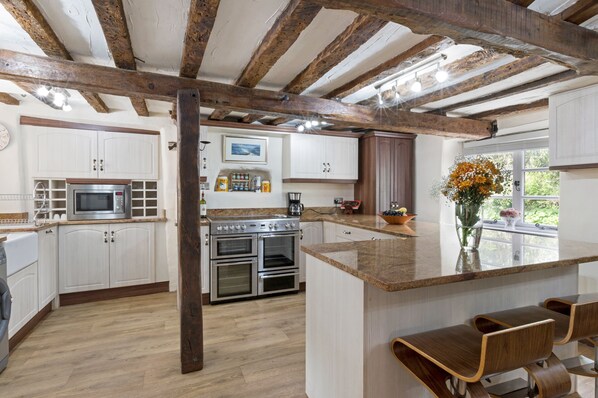A kitchen with white cabinets, a central island, wooden beams, and a view of greenery outside. - Thorn Cottage. A quaint 300 year old cottage in a rural village. Dog friendly (Newton abbot)