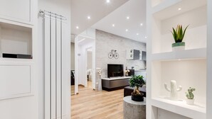 Una sala de estar moderna con televisor, sofá y zona de comedor con cocina al fondo.