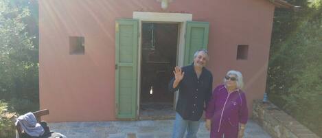 A small pink building with a door and windows, a chair outside, and a person waving.