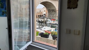 Ikkunasta avautuu näkymä sisäpihalle, jossa on veneitä, kivinen holvikaari ja kyltti, jossa lukee ”MOTEL”.