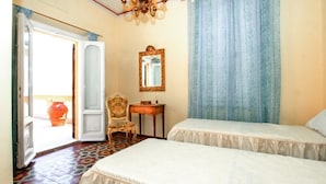 Una habitación con dos camas, una silla, una mesita, un espejo y una puerta que da al exterior.