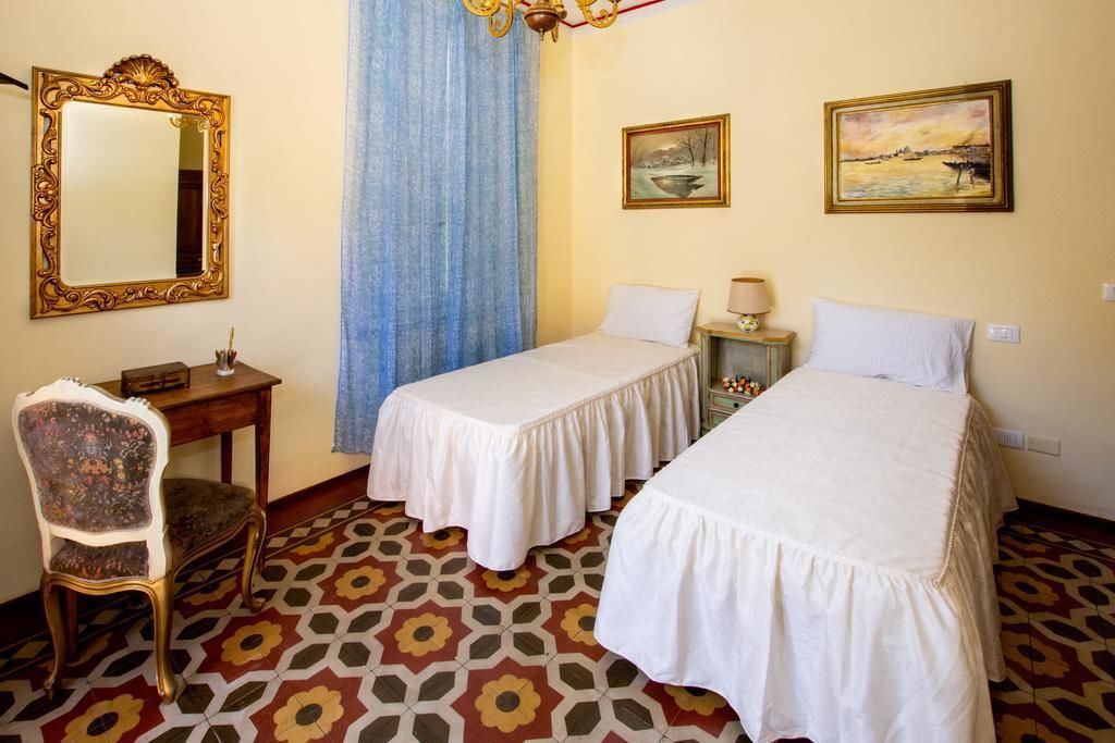 A hotel room with two beds, a desk, a chair, a mirror, and two paintings on the wall.
