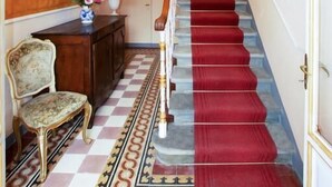 Una imponente escalera con alfombra roja, un candelabro y un suelo estampado.