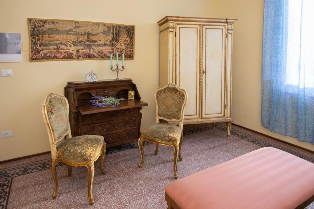 Een kamer met twee versierde stoelen, een houten kast, een groot schilderij en een bed.