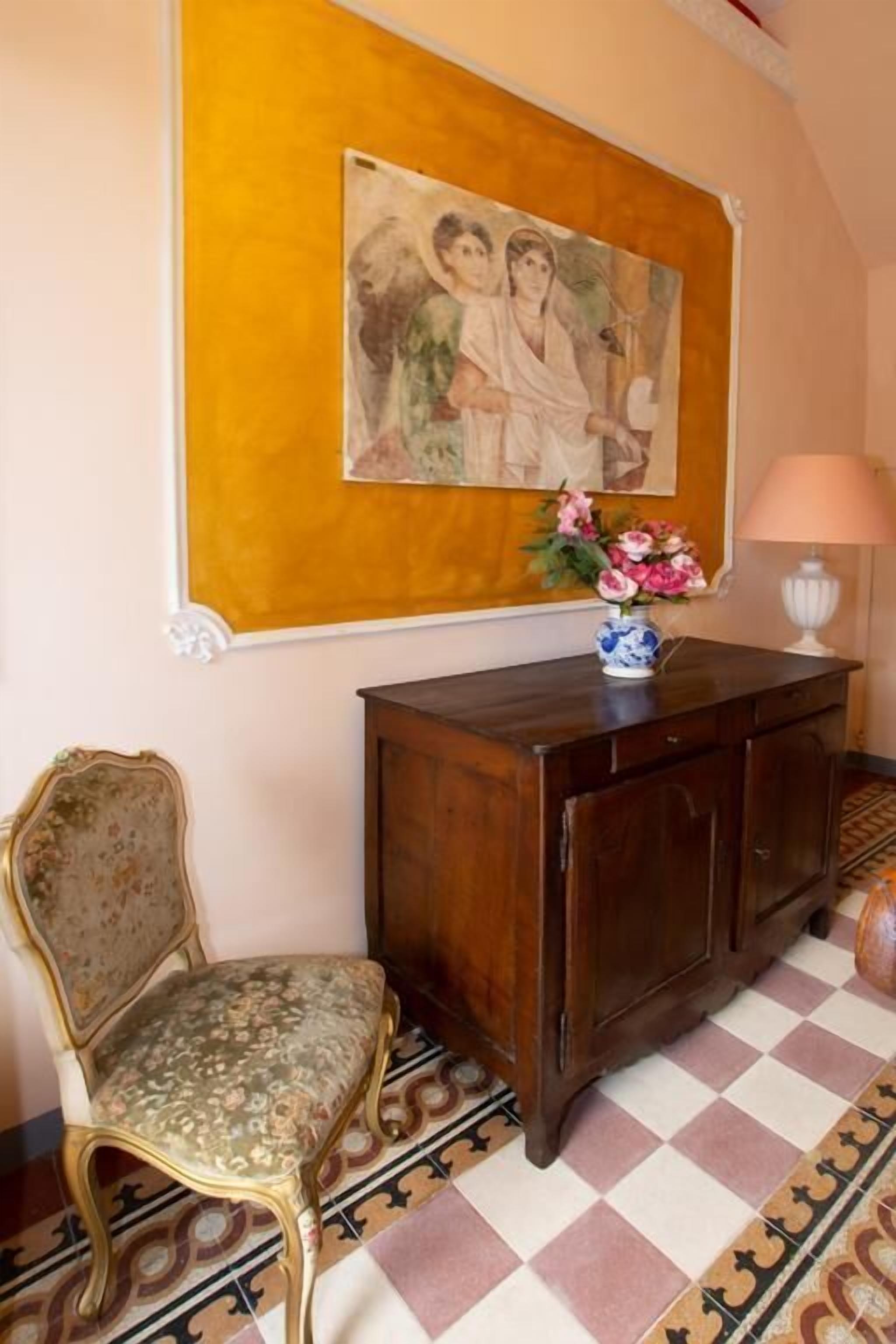 A room with a patterned floor, a wooden cabinet, a chair, and a framed painting on the wall.