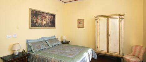 Une chambre à coucher comprenant un lit, une table de chevet, une commode, une chaise et un lustre.