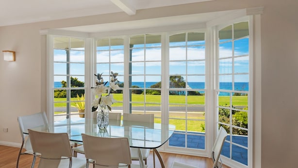 A dining area with a glass table and chairs, large windows with a view of the ocean and greenery. - 31 McMillan Crescent, Dalmeny (Dalmeny)