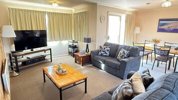 Ein Wohnzimmer mit Flachbildfernseher, einer Couch, einem Couchtisch und einem Essbereich mit Tisch und Stühlen.
