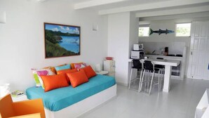 Una habitación luminosa con una cama, un escritorio y una zona de cocina.