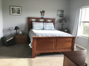A bedroom with a wooden bed, two nightstands, a dresser, and a window with curtains.