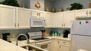 Une cuisine avec des meubles blancs, un four à micro-ondes, une cuisinière, un évier et un réfrigérateur.
