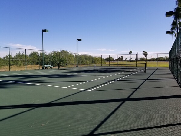 An outdoor tennis court with a net, benches, and a fence.
