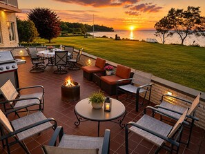An outdoor patio with a grill, seating, and a view of the sunset over water.