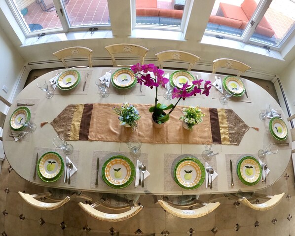 A dining table set for eight with green and yellow plates, silverware, and glassware, surrounded by chairs.