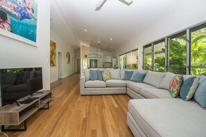A modern living room with a sectional sofa, a flat-screen TV, and a wooden coffee table. - Whispering Palms (Nelly Bay)