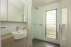 A bathroom with a white sink, a glass shower enclosure, and a window with blinds.